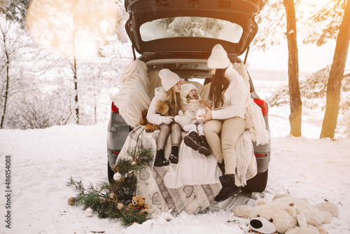 Mother and daughters. Mom and daughters drink hot chocolate in the car. Family trip in the winter forest.  Christmas holiday in the mountains.