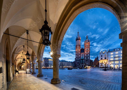Krakow main square with view on St mary's basilica under illuminated gothic arches during overcast blue hour