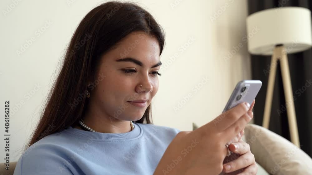 Close up of beautiful and happy, smiling young teenage girl sit at sofa. Interact with phone application, scroll and text on screen. Use social media or online shopping. Content phone user. 4k footage Close up of beautiful and happy, smiling young teenage girl sit at sofa. Interact with phone application, scroll and text on screen. Use social media or online shopping. Content phone user. 4k footage