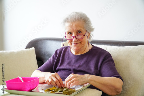 Old woman preparing traditional stuffed grape leaves food. Old woman rolling stuffed grape leaves. Traditional Turkish food yaprak sarma. Woman making zeytinyağlı yaprak sarma.  photo