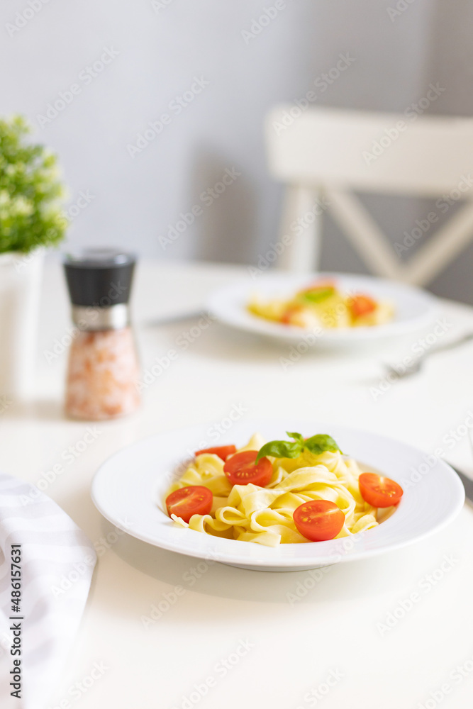 Italian pasta with cherry tomatoes, tomato sauce and cheese, garnished with a sprig of basil. Ready lunch or dinner. Table setting