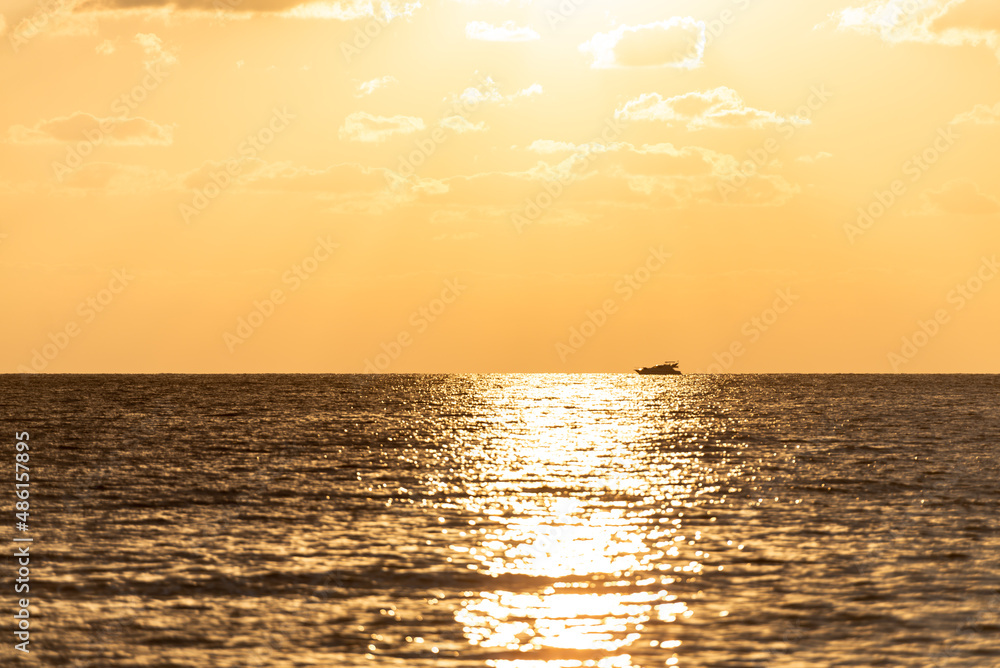 Sunset path on the sea with a ship. Orange colors of the low sun in the Mediterranean Sea.