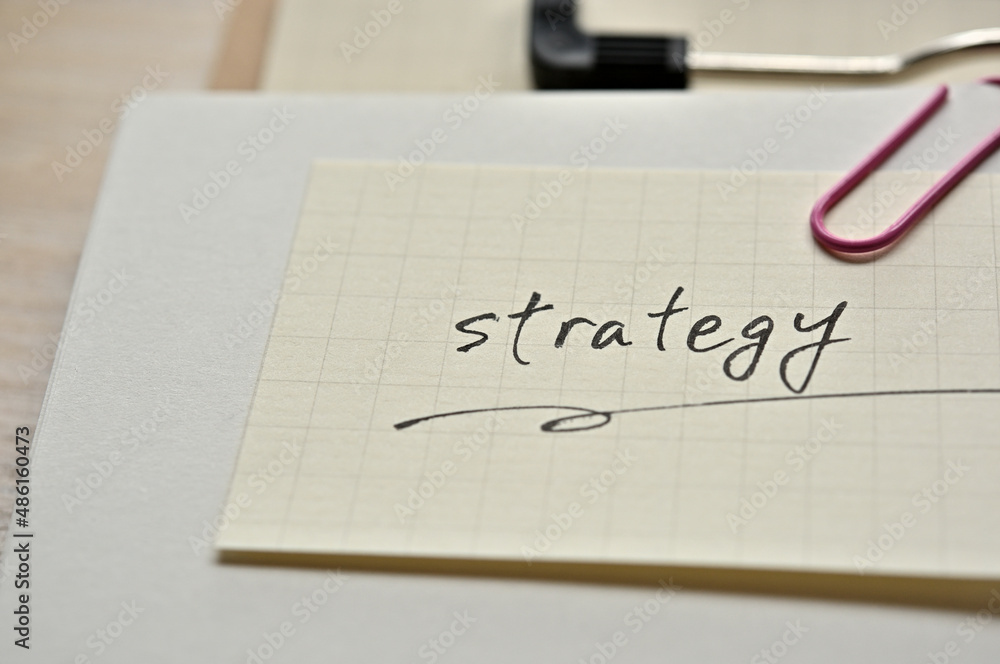 A piece of paper clipped to the edge of the notebook has Strategy. A piece of paper clipped to the edge of the notebook has Strategy.
