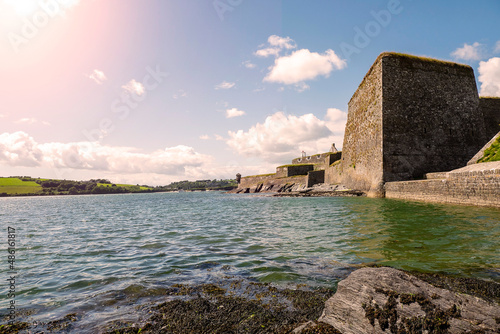 Stone wall of Fort Charles, Kinsale town, Ireland. Warm sunny day, cloudy sky. Blue ocean water. Powerful fortification to protect harbor. Popular history museum and tourist landmark. photo
