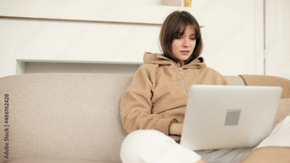 Smiling young woman sitting on couch using laptop. Happy young woman relaxing on sofa with computer, working at home. High quality 4k footage
