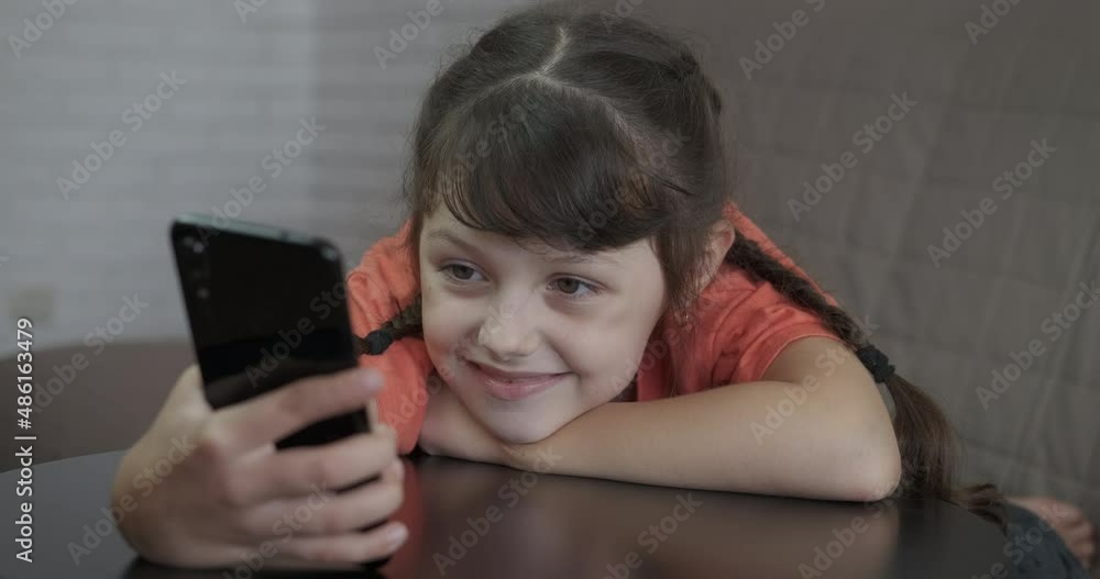 Curious child with smartphone. A curious little girl hold her eyes only on telephone screen in the room.