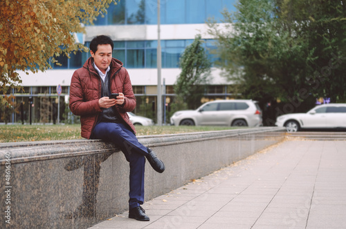 Middle aged asian man sitting on the bench with phone.