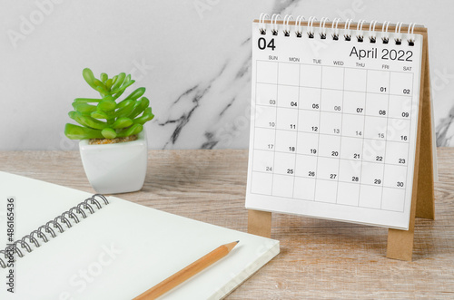 April 2022 desk calendar with plant on wooden table.