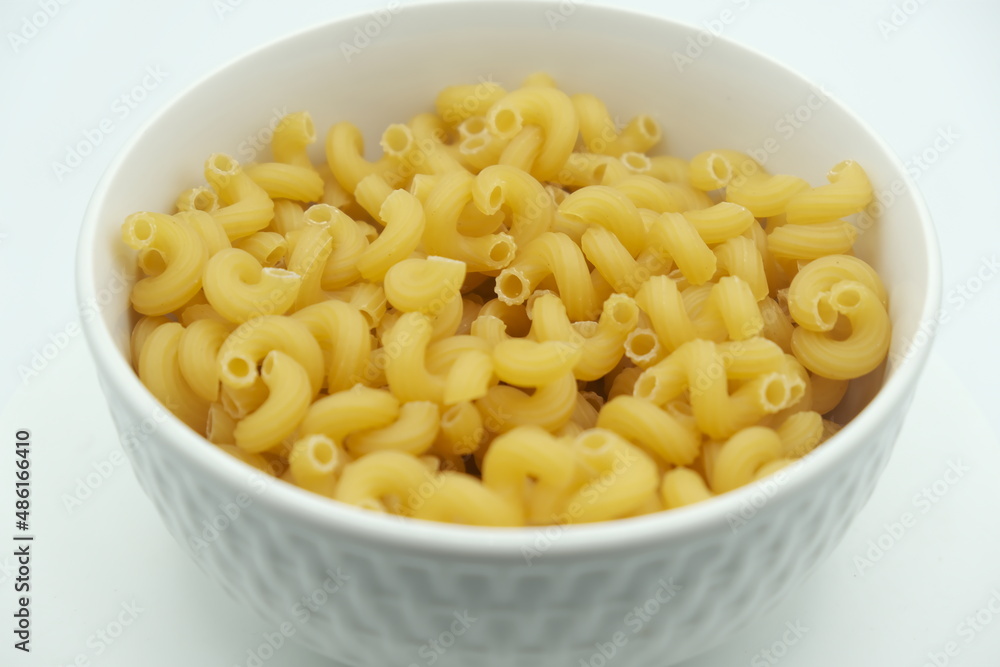 Raw macaroni in white bowl on white background Raw macaroni in white bowl on white background