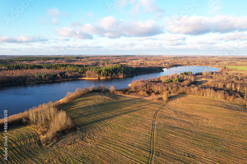 Lake on sunset in autumn season. Aerial panoramic landscape view of lake in wild. Drone view of agricultural field at lake in spring. Wetland in fall color. Arable land ploughed. Clouds sky background