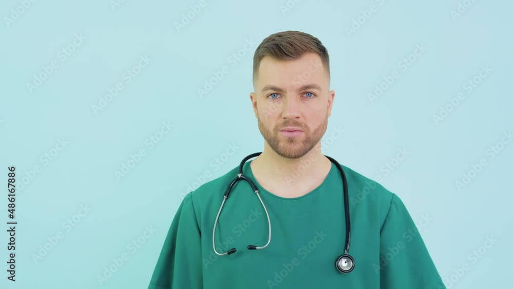 Successful doctor surgeon in green uniform, blue gloves and stethoscope looks at camera on blue background Successful doctor surgeon in green uniform, blue gloves and stethoscope looks at camera on blue background