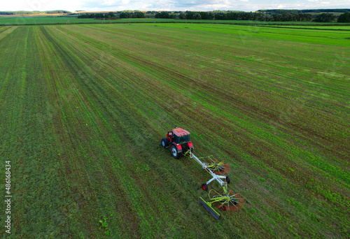 Tractor raking grass for silage harvesting. Agriculture farm machinery work at field. Cutting grass silage at farm field. Wheel Rakes for Grass silage raking, baling, wrapping. Hay making for cattle. 