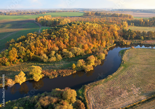 River at field in the fall season. Golden autumn landscape. Aerial view of the wild river on sunset in autumn season. Trees with yellow leaves at a small winding river. Aerial panoramic landscape.