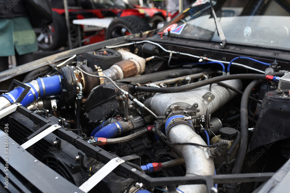 Sports car engine with turbine. An open race car hood on a pit stop while racing on a race track. Motor with turbocharger. Boos and tunning. Sports car engine with turbine. An open race car hood on a pit stop while racing on a race track. Motor with turbocharger. Boos and tunning.