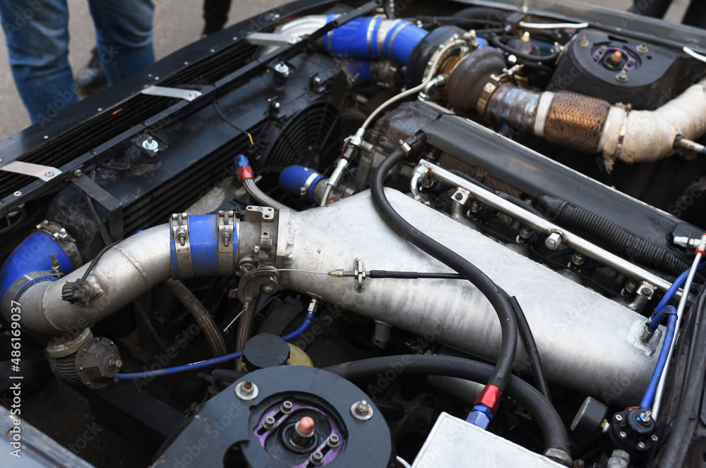 Sports car engine with turbine. An open race car hood on a pit stop while racing on a race track. Motor with turbocharger. Boos and tunning. Sports car engine with turbine. An open race car hood on a pit stop while racing on a race track. Motor with turbocharger. Boos and tunning.