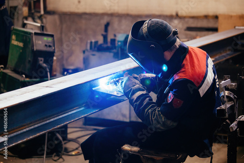 Factory worker in protective mask welding iron parts, close up