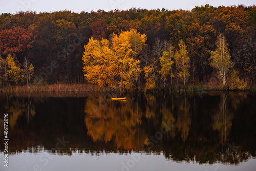 Yellow small boat near the forest with golden autumn trees