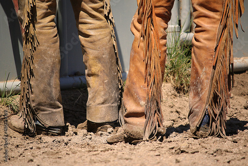 Western lifestyle rearview image of the lower legs of two cowboys wearing leather chaps and cowboys boots covered in mud. photo