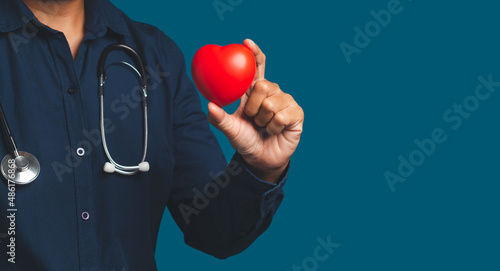 Hand of a doctor holding a red heart shape while standing on a blue background.