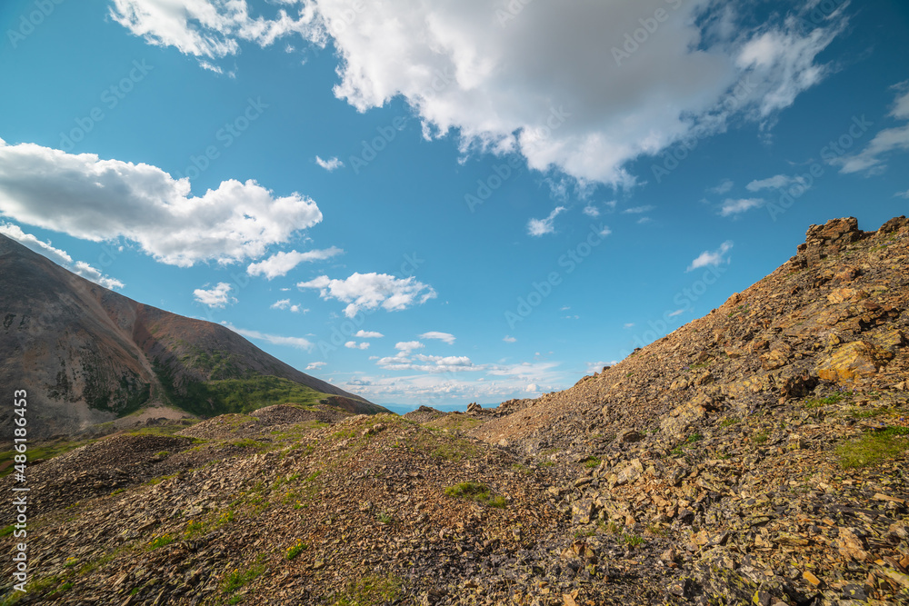 Scenic landscape with sunlit mountain pass under clouds in blue sky in sunny day. Colorful mountain scenery with stone hills in bright sun under cloudy sky in changeable weather. Mountains in sunlight