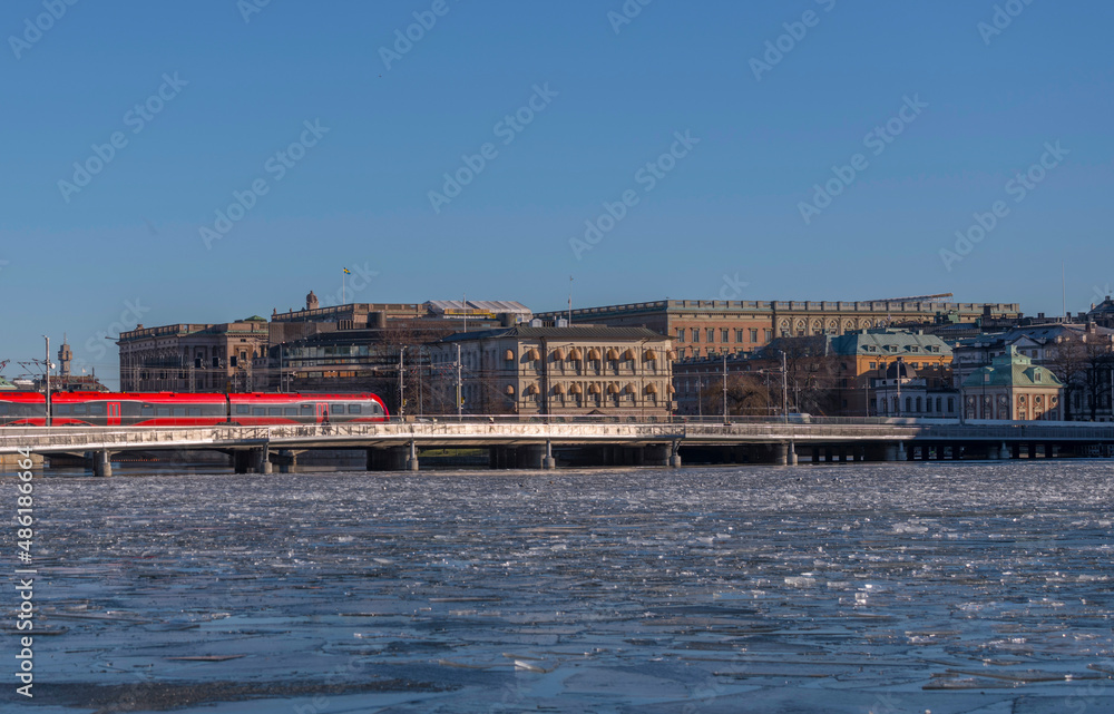 Panorama view, a train on a bridge leaving the central station at the bay Riddarfjärden with ice floes, background with government houses and the royal castle a sunny winter day in Stockholm