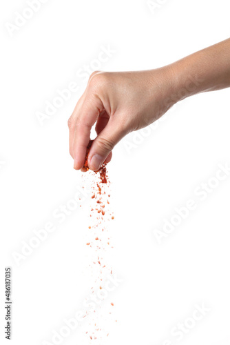 Hand sprinkling cayenne pepper on white background