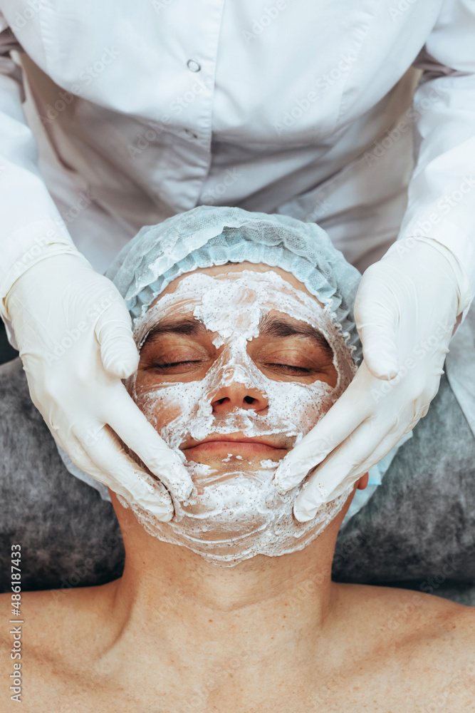 Beautician applying scrub mask on face to young man, spa beauty salon. The concept of body and face care for men Beautician applying scrub mask on face to young man, spa beauty salon. The concept of body and face care for men