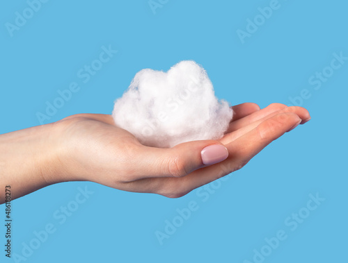 Hand holding cotton cloud at blue sky background. Dreaming or weather concept in surrealism style. High quality photo