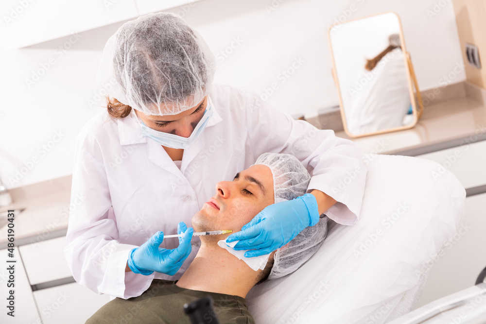 Obraz premium Focused woman cosmetologist giving beauty injections for face skin tightening for male client in aesthetic medicine office