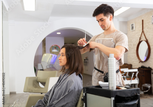 Portrait of young man hairdresser applying color to woman's hair during hair dye colouring in salon