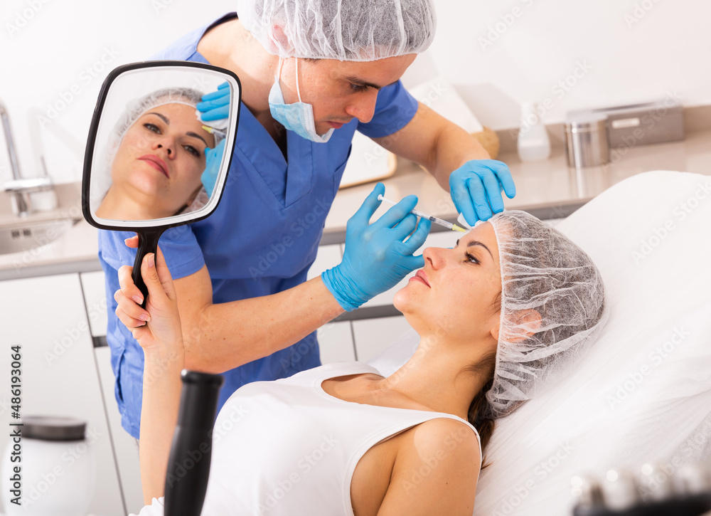 Obraz premium Young woman patient of beautician receiving rejuvenating facial injections, concept of aesthetic medicine