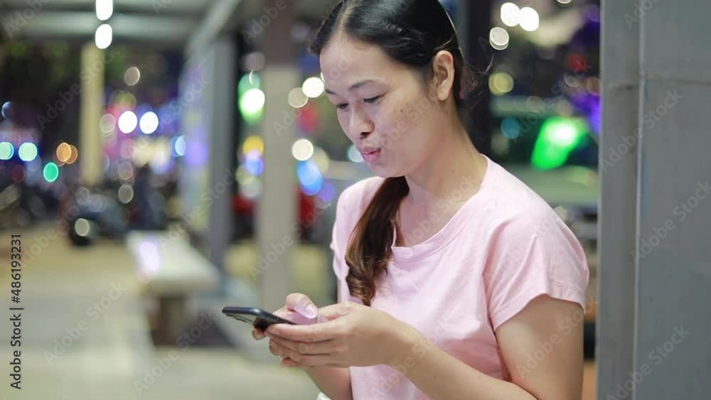 Asia woman holding smartphone looking down screen at night city face illuminated by screen light - communication concept technology Asia woman holding smartphone looking down screen at night city face illuminated by screen light - communication concept technology