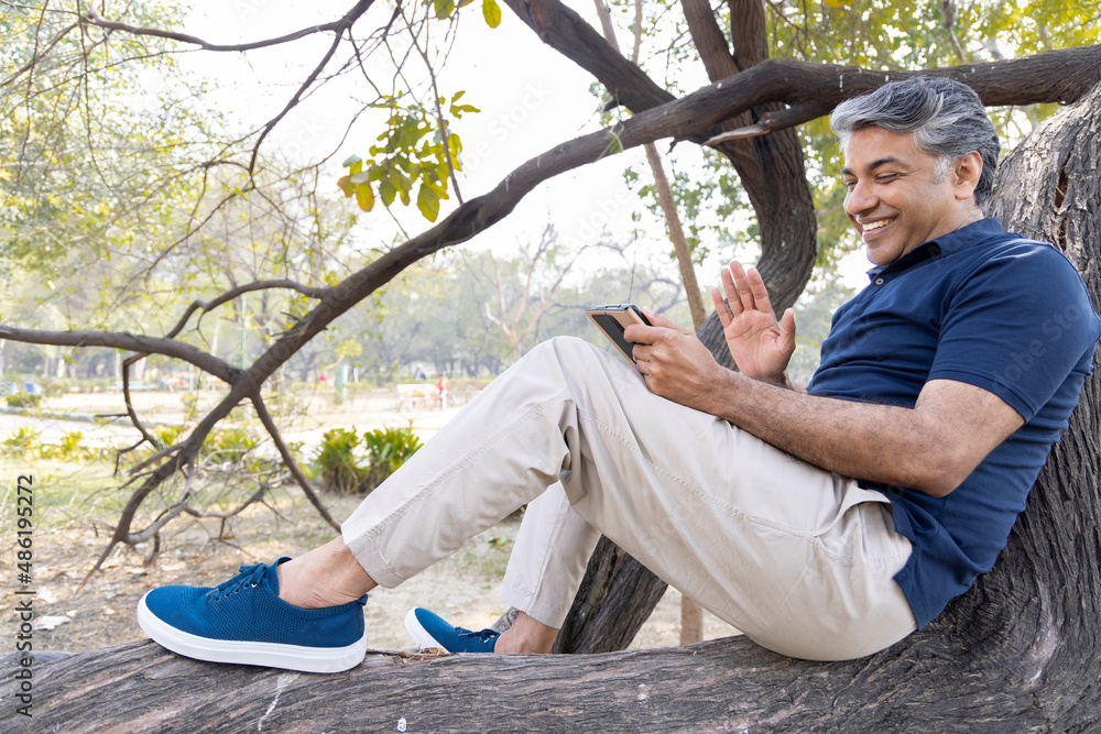 Cheerful mid adult man talking using mobile phone at park Cheerful mid adult man talking using mobile phone at park