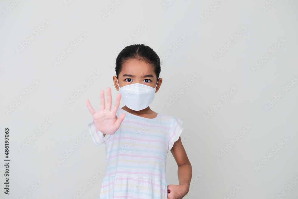 Asian kid wearing medical mask looking angry and give stop hand sign Asian kid wearing medical mask looking angry and give stop hand sign