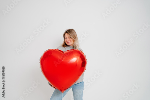 an blonde woman with a large red heart-shaped balloon on a white background. valentine's day © andrey