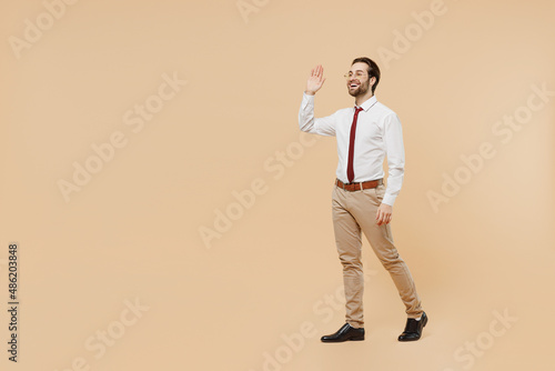 Full body side view fun young successful employee business man corporate lawyer 20s wear white shirt red tie glasses work in office walking going waving hand isolated on plain beige background studio.