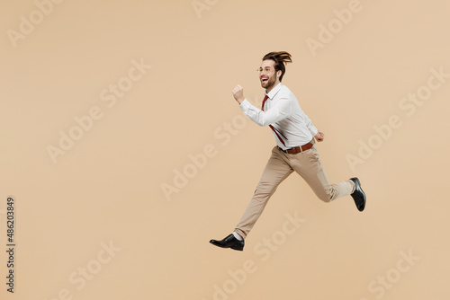 Full body side view young successful employee business man corporate lawyer 20s wear white shirt red tie glasses work in office run fast jump high isolated on plain beige background studio portrait.