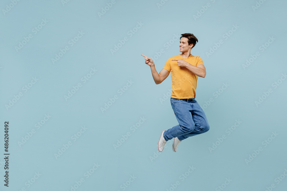 Full body happy young man 20s wear yellow t-shirt jup high point index finger aside on workspace area mock up isolated on plain pastel light blue background studio portrait. People lifestyle concept. Full body happy young man 20s wear yellow t-shirt jup high point index finger aside on workspace area mock up isolated on plain pastel light blue background studio portrait. People lifestyle concept.