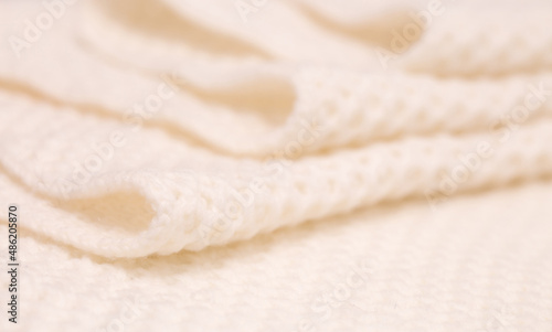 Knitted surface of woolen things as a background. Close-up of soft white texture of knitted patterns. Warm winter clothes. Background textile surface with copy space for text.