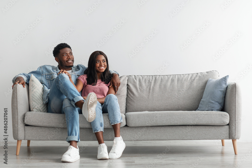 Happy black couple spending weekend together sitting on couch