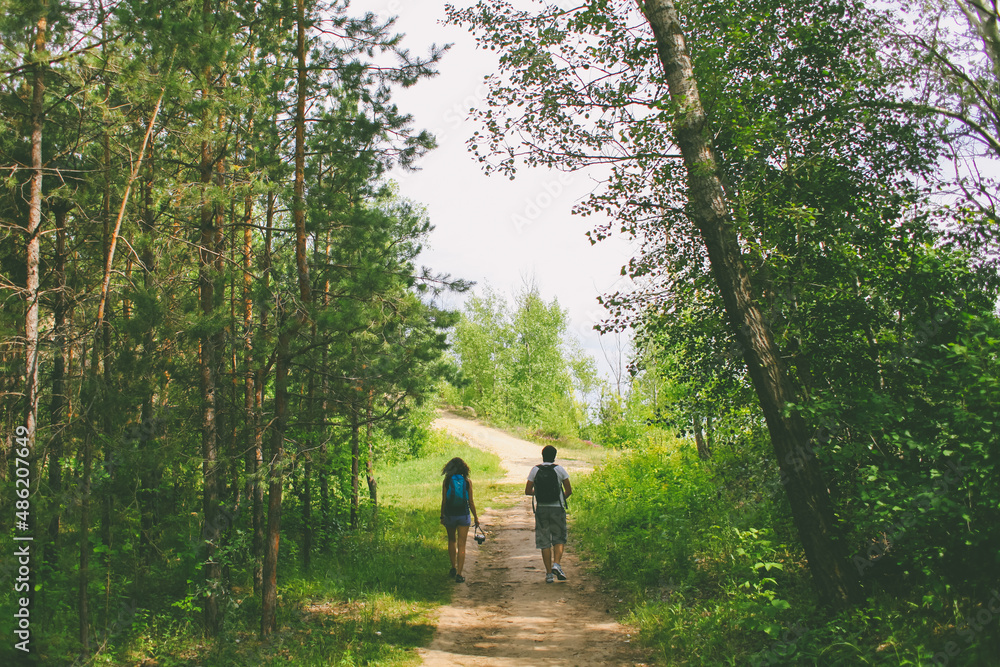 Fototapeta premium a couple of young people with backpacks walking along a forest path in summer