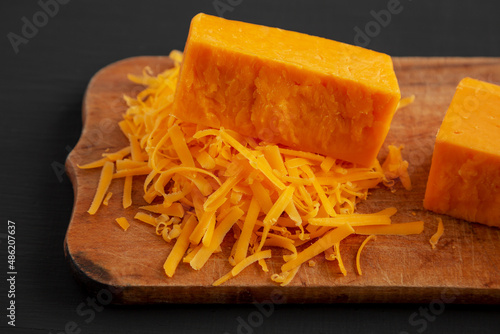 Shredded Sharp Cheddar Cheese on a rustic wooden board on a black background, side view.