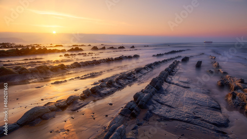 Warm sunset at Barrika beach with several rows of rocks directing the gaze towards an oil tanker