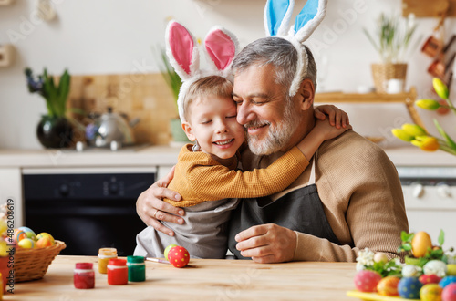 Happy family loving grandfather and cute little boy grandson embracing while painting Easter eggs