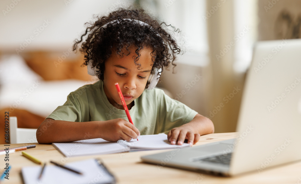 Smiling african american child school boy in headphones studying online on laptop at home Smiling african american child school boy in headphones studying online on laptop at home
