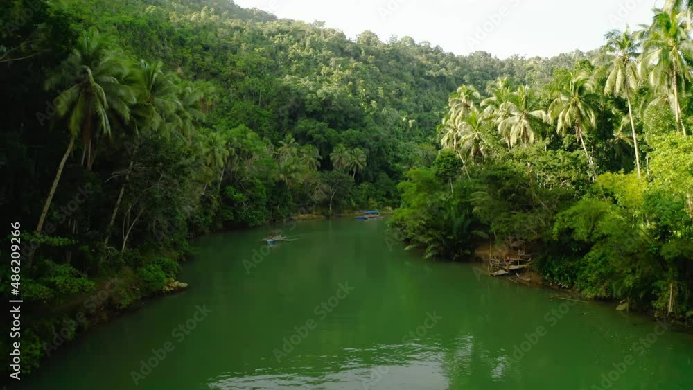 Calm Loboc river in Bohol province where traditional filipino boats move tourists across the vast green jungle of the Philippines on a sunny day. Low angle drone dolley shot