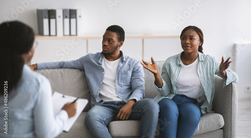 Female psychologist giving therapy session to stressed young black couple at office, panorama