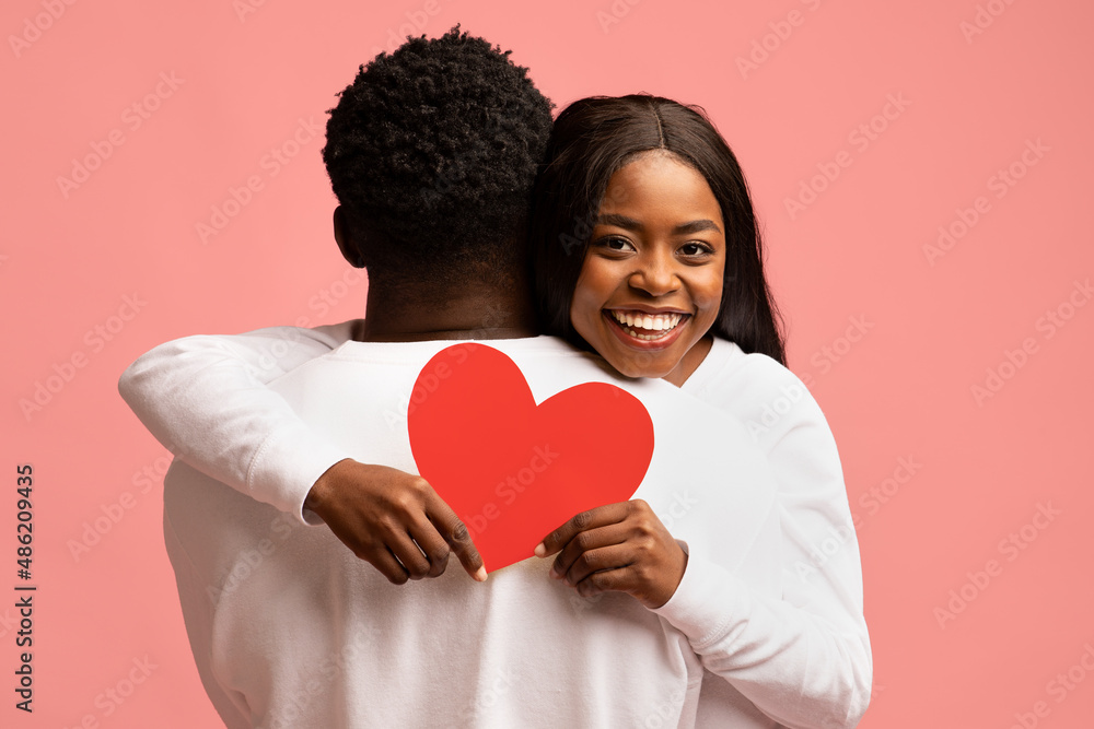 Happy african american lady hugging her boyfriend, holding red heart Happy african american lady hugging her boyfriend, holding red heart