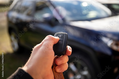 A close up portrait of a person standing next to a car holding a car key in his hand pressing the unlock button. the remote control has unlock, lock icons for the doors and the trunk of the vehicle.