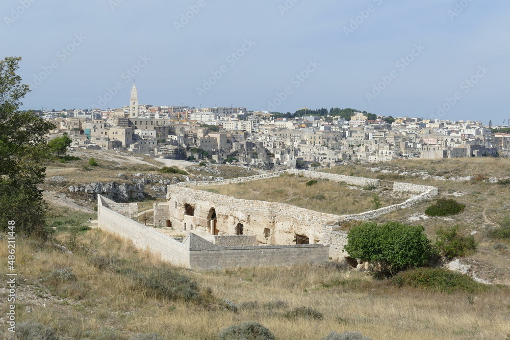 San Falcione rupestrian church in Murgia Materana Park surrounded by a stone perimeter wall with the canyon and Matera old town in the background